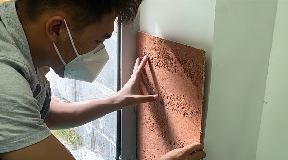 Worker using a blade to adjust the position of a flexible stone tile during installation.